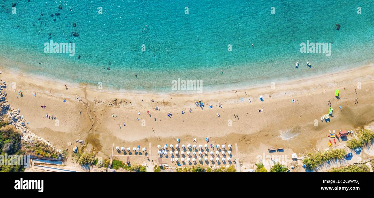 Vista aerea dall'alto della bellissima spiaggia di Coral a Paphos con acque marine azzurre, Cipro. Costa di sabbia con ombrelloni, lettini, persone e acqua di mare limpida. Foto Stock