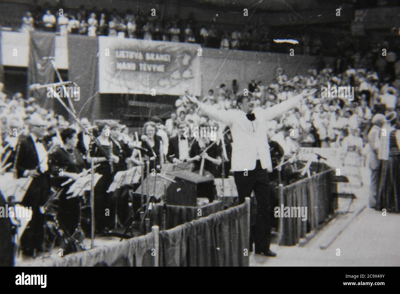 Bella fotografia in bianco e nero degli anni '70 di un conduttore che indossa un tuxedo che si inzuppa al pubblico. Foto Stock