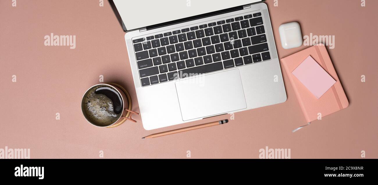 Vista dall'alto dello spazio di lavoro femminile con computer portatile, diario, accessori, tazza da caffè e spazio per la copia su un tavolo rosa Foto Stock