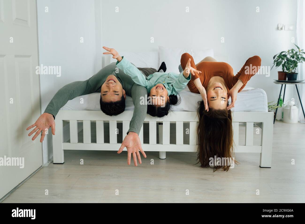 Allegra madre e padre asiatici con figlia giovane che si trova sul letto e guardando la macchina fotografica. Concetto di "togetherness e bonding indoor" per la famiglia Foto Stock