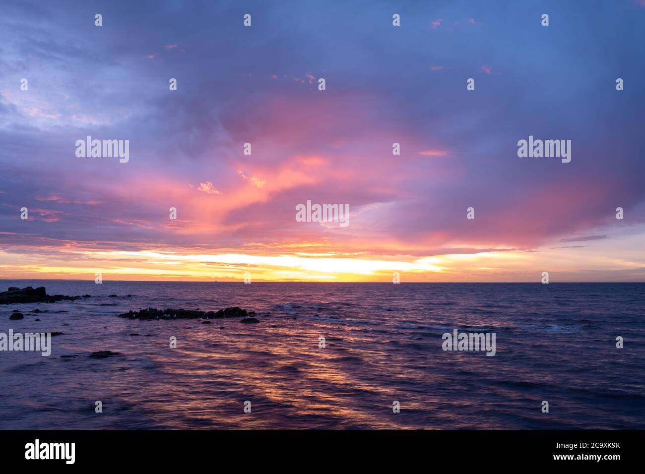Tramonto luminoso sulla costa dell'oceano con rocce e gabbiani Foto Stock