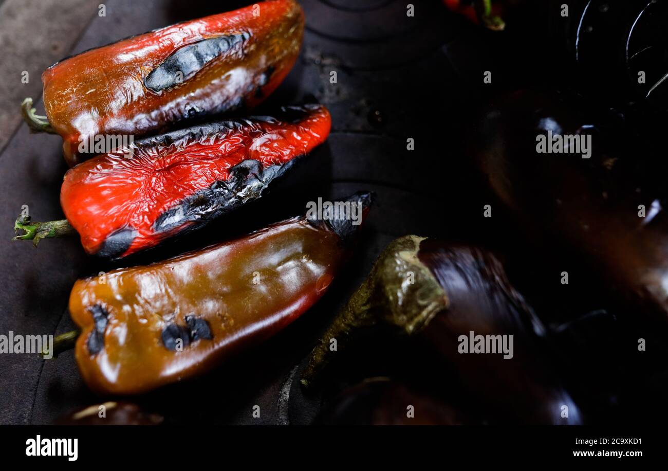 Dettagli con paprica rossa arrostita e melanzane in cima ad una stufa in metallo all'aperto con fuoco a legna. Foto Stock