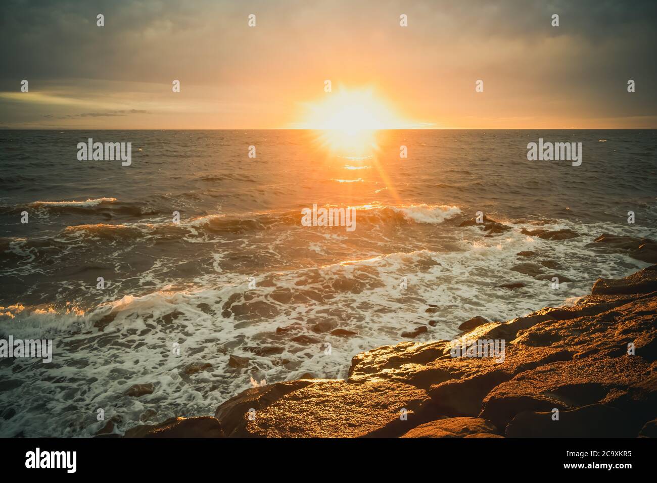 Tramonto sull'acqua con onde e rocce Foto Stock