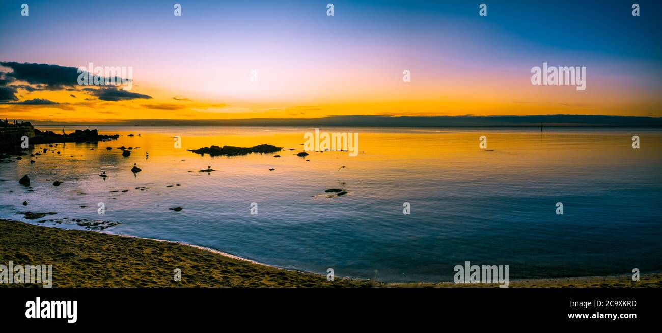 Mare panoramico di un tramonto luminoso sulle calme acque della baia dell'oceano con rocce e silhouette di uccelli Foto Stock
