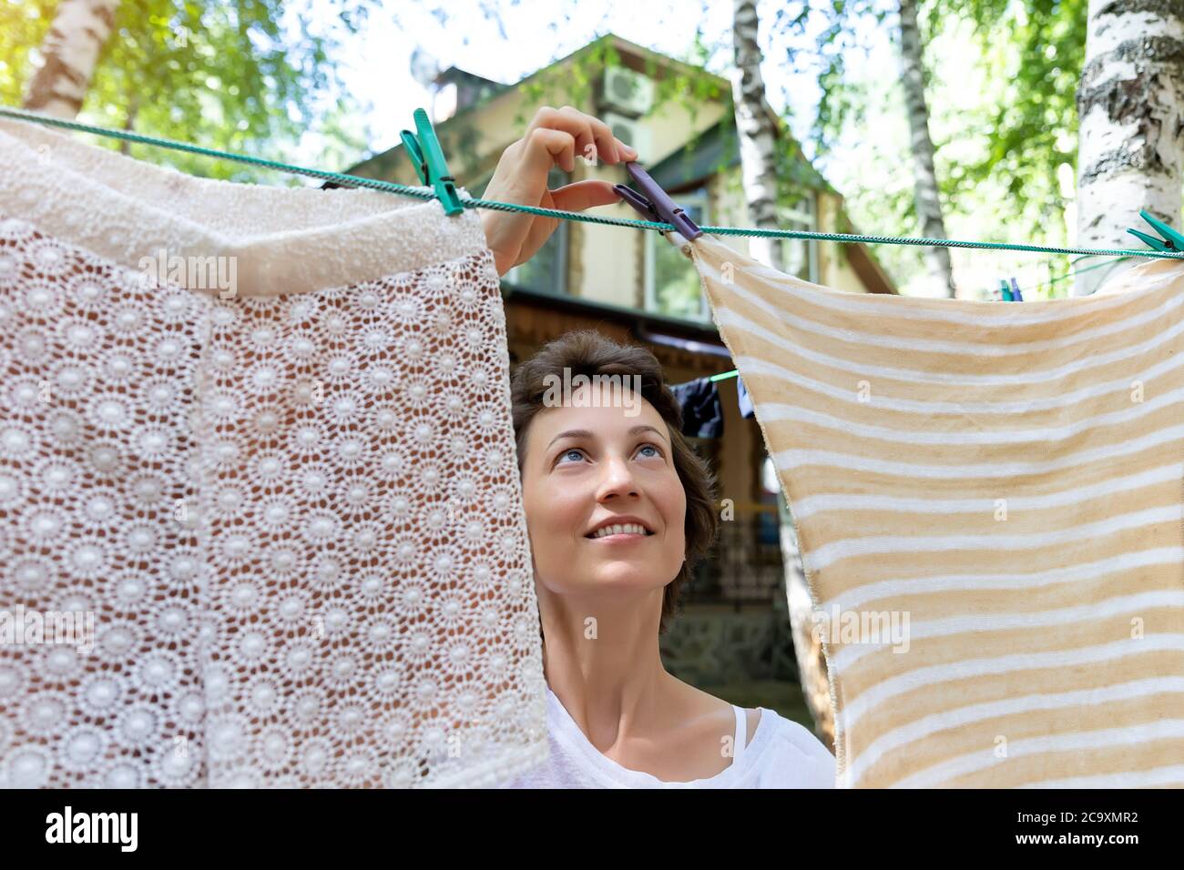 Ritratto di vita reale candida di giovane adulto bella donna caucasica  attraente appesa su vestiti di famiglia freschi lavati su vestito di  betulla con Foto stock - Alamy