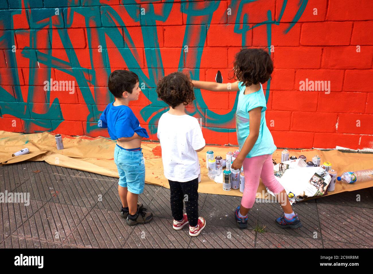 Tre bambini che guardano colorati graffiti dipinti su una parete bianca Foto Stock