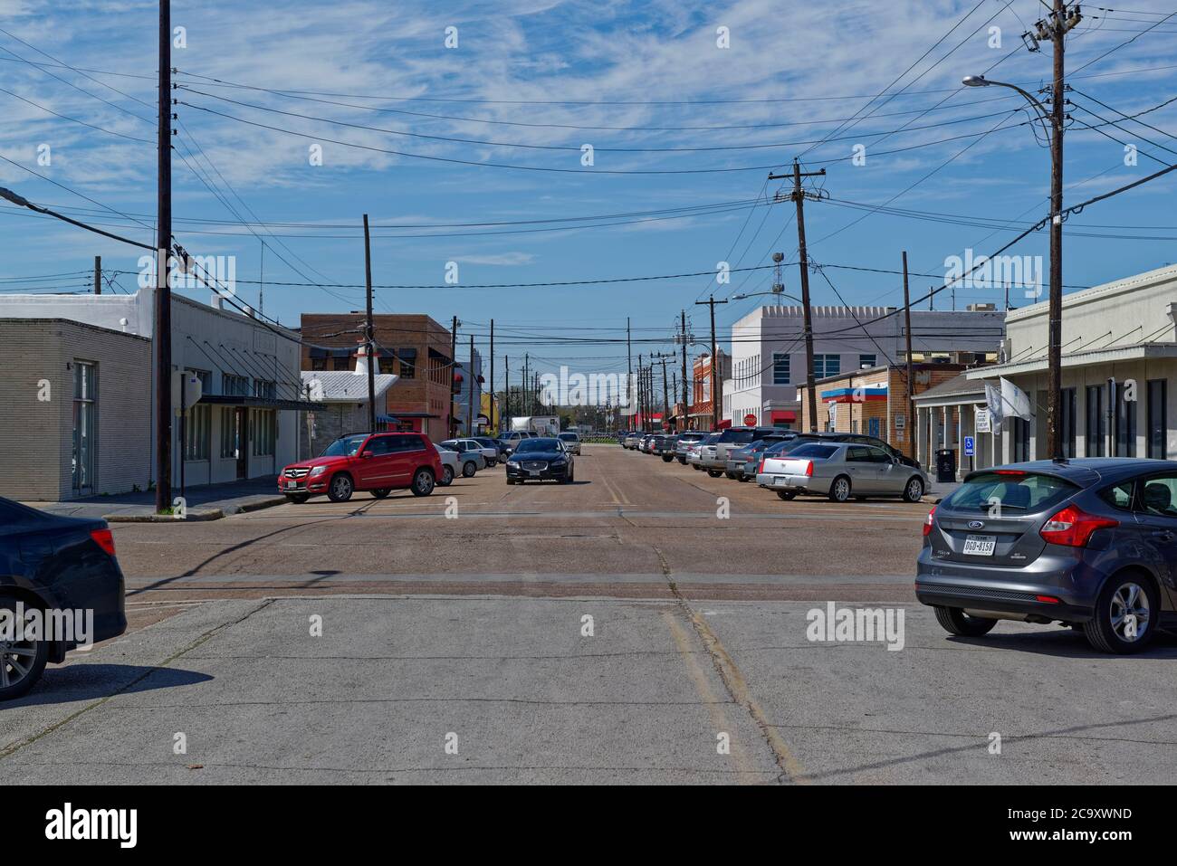 Guardando lungo una strada diritta a Rosenberg, Texas, con auto parcheggiate, e una Jaguar Car sulla strada in una giornata di sole a marzo. Foto Stock