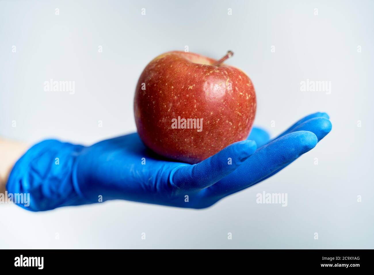 mano guanto che tiene una mela rossa, protezione contro il coronavirus Foto Stock