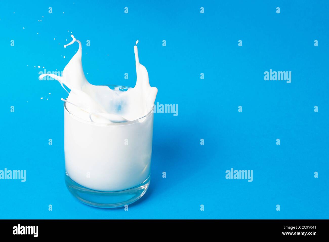 Gocciolamento di latte, un bicchiere di latte. Su sfondo blu. Vista dall'alto. Disposizione piatta. Foto Stock