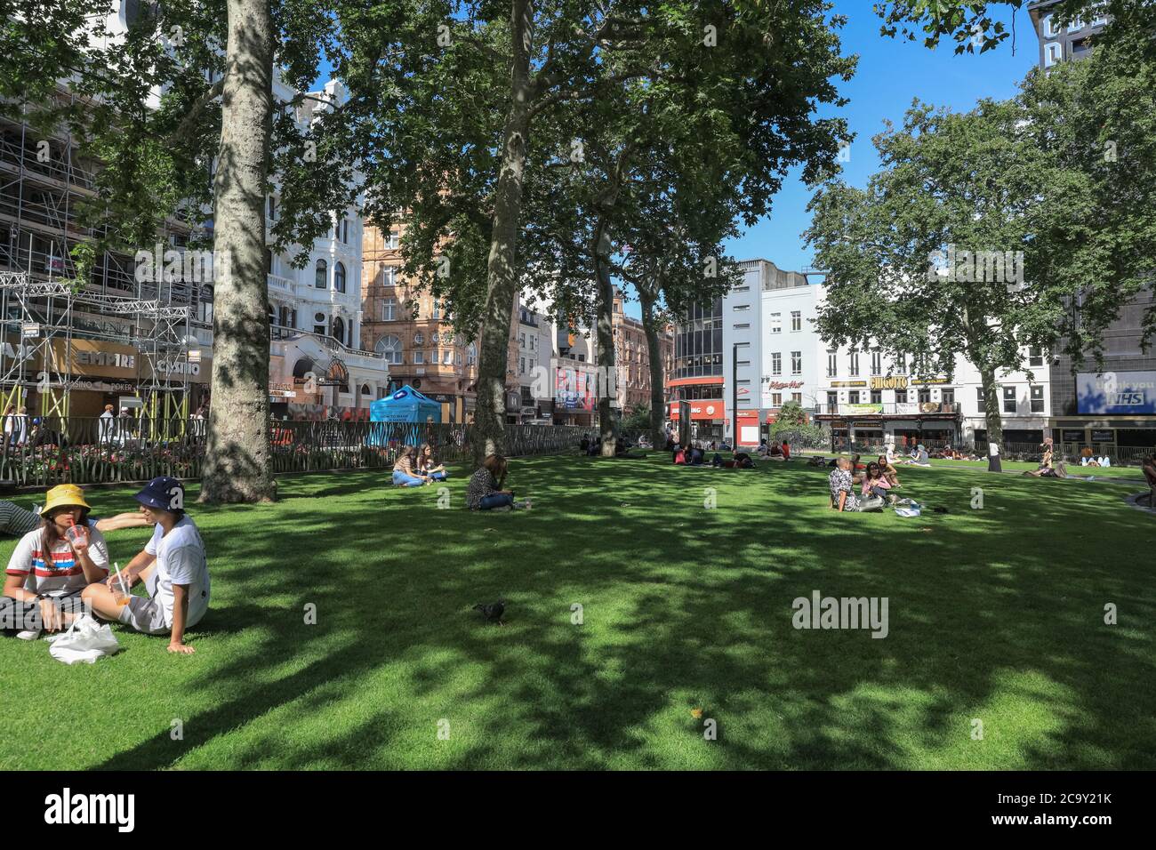 La gente siede nei giardini di Leicester Square in estate, spazio verde pubblico a Soho, Londra, Inghilterra, Regno Unito Foto Stock