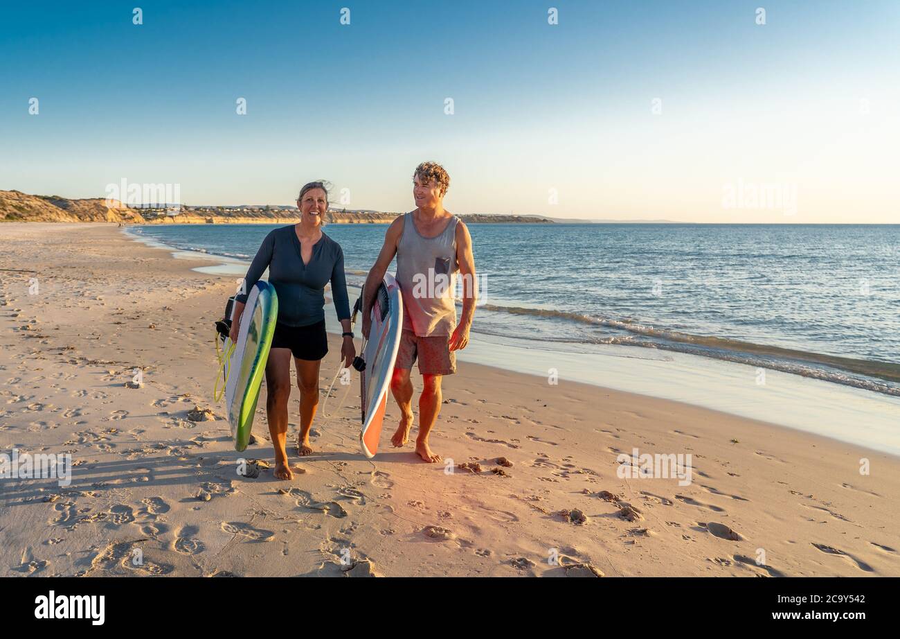 Coppia matura con tavole da surf sulla bellissima spiaggia godendo di paradiso e di uno stile di vita attivo. Bella forma uomo e donna surf e divertirsi. In trave Foto Stock