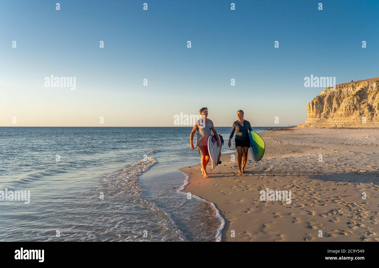 Coppia matura con tavole da surf sulla bellissima spiaggia godendo di paradiso e di uno stile di vita attivo. Bella forma uomo e donna surf e divertirsi. In trave Foto Stock