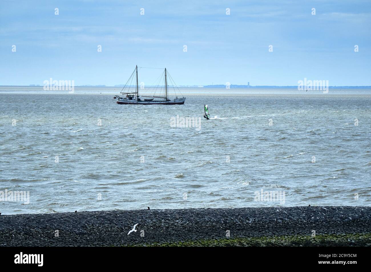 Harlingen, Paesi Bassi, 23,2020 luglio: Wadden mare con windsurf e vecchia nave a vela tradizionale, diga in pietra nera, molo e all'orizzonte il Foto Stock