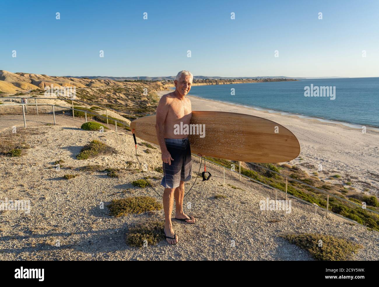 Attraente uomo australiano maturo surfer con fresco surf vintage sulla spiaggia al tramonto. Adulto anziano felice di essere di nuovo al surf . L'avvento dello sport all'aperto Foto Stock