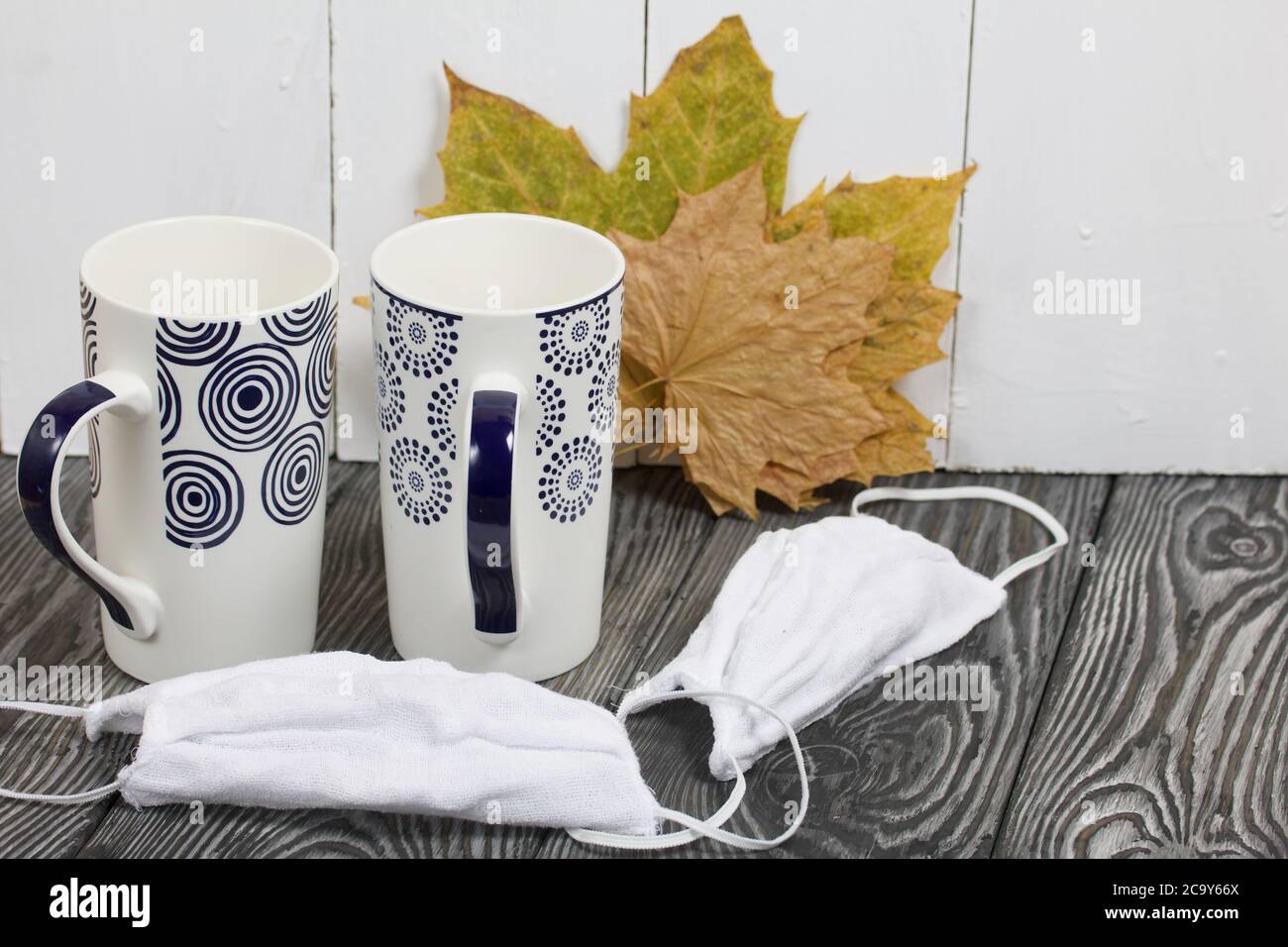 Due tazze in ceramica. Prima di loro sono maschere protettive per la durata della pandemia. Dietro di loro si asciugano foglie d'acero d'autunno. Foto Stock