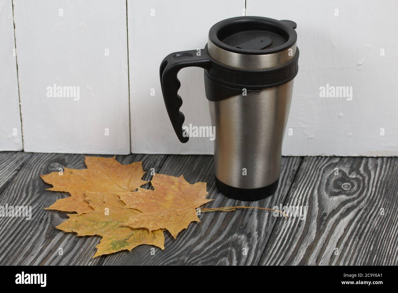 Tazza termica su una superficie di legno di pino. Nelle vicinanze si trovano foglie di acero essiccate. Foto Stock