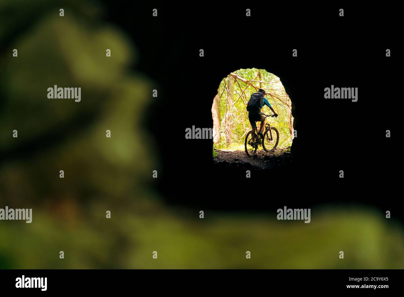 ciclista con zaino e mountain bike che parte alla fine di un tunnel, concetto di sport e stile di vita sano in natura, copia spazio per il testo Foto Stock