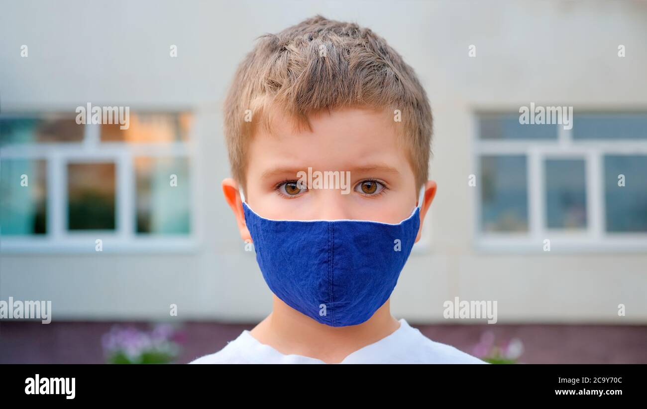 Maschera da indossare turistica. Il viso di un ragazzo caucasico indossa una maschera medica a scuola sullo sfondo della città. Un ragazzo bei occhi. Occhi dei bambini. Giovane Foto Stock