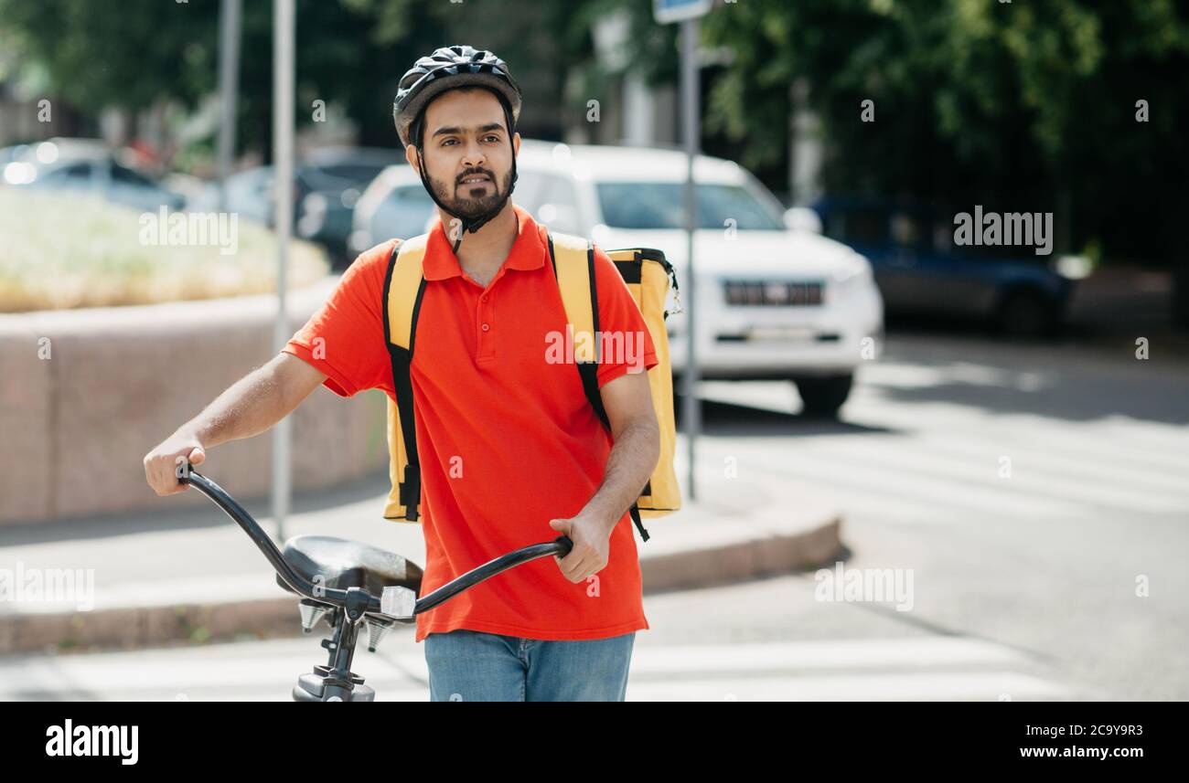 Consegna a casa o in ufficio. Giovane uomo in casco protettivo con zaino in bicicletta alla ricerca dell'indirizzo del cliente Foto Stock