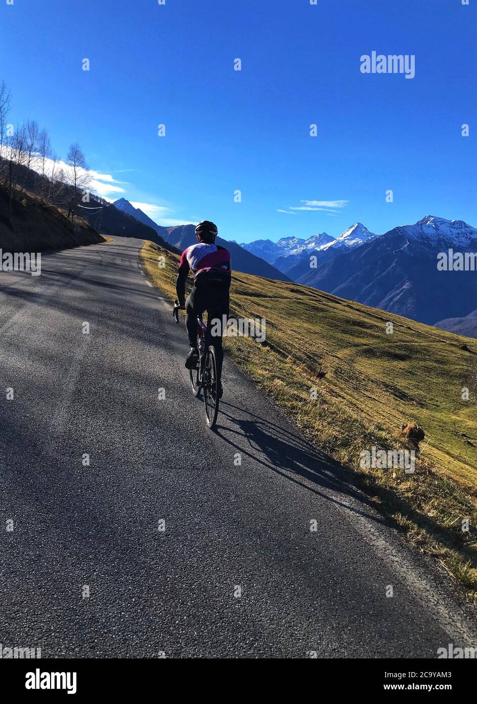 Tiro verticale di un maschio che cavalcano una bicicletta su a. lunga strada in un campo di montagna Foto Stock