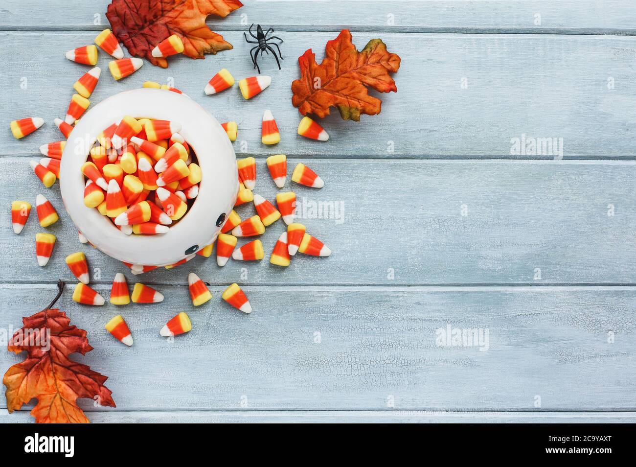 Halloween Holiday Candy mais in una ciotola fantasma generica e decorazioni su uno sfondo di legno blu con spazio libero per il testo per Trick o trattare. Vi Foto Stock