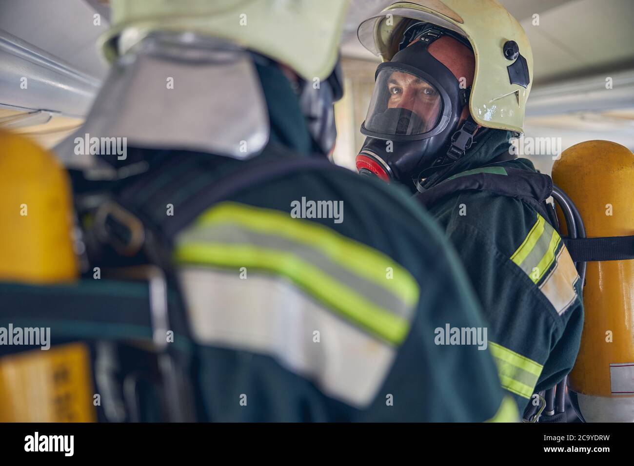 Due vigili del fuoco con attrezzature complete in piedi nel luogo di emergenza Foto Stock