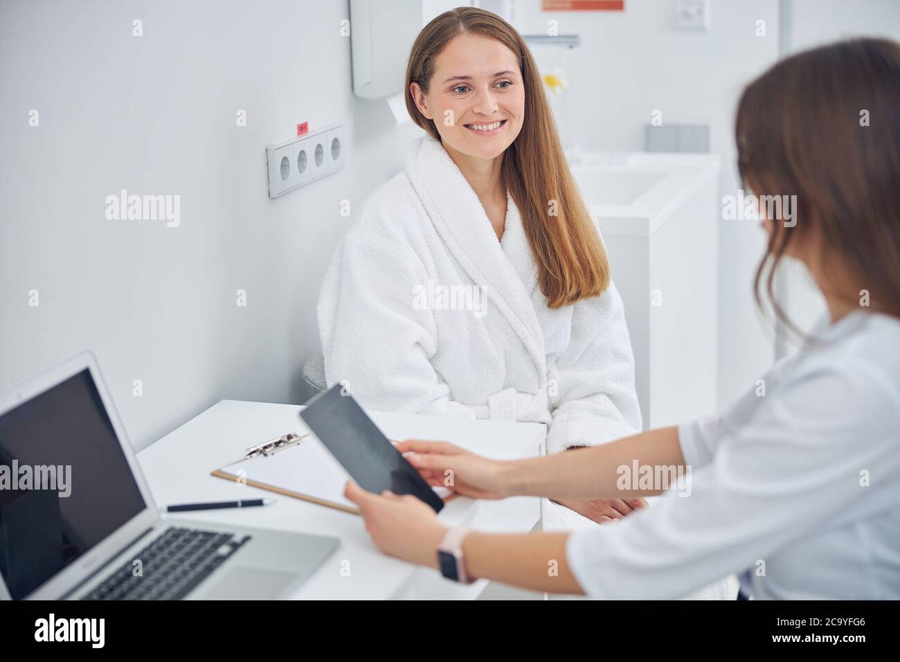 Sorridente bella signora in bianco morbido accappatoio che riceve la consultazione dal medico Foto Stock