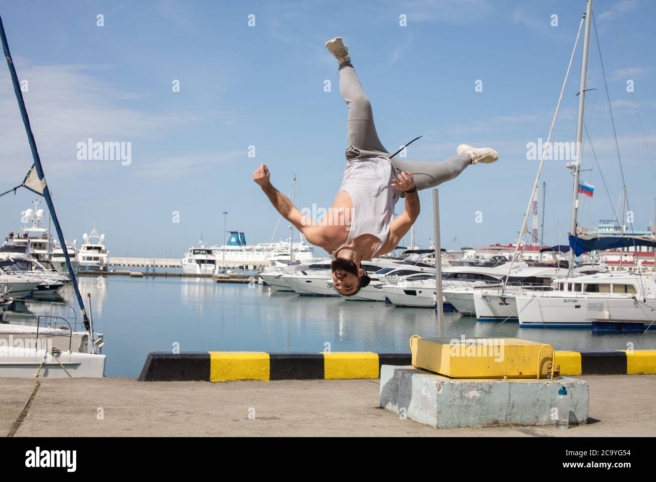 Closeup di muscoloso sportivo in crossfit facendo flip salto esercizio all'aperto, volare l'uomo contro il molo di mare con sfondo marina. Foto Stock