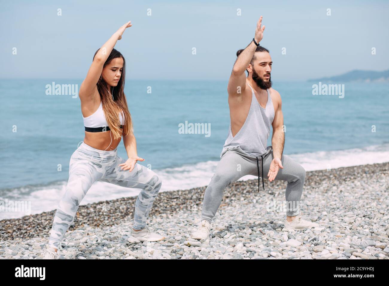 Pugile o combattente femminile professionista e il suo allenatore che si scaldano all'aperto, facendo taekwondo esercizio insieme sulla spiaggia di ghiaia oceano con mare surf A. Foto Stock