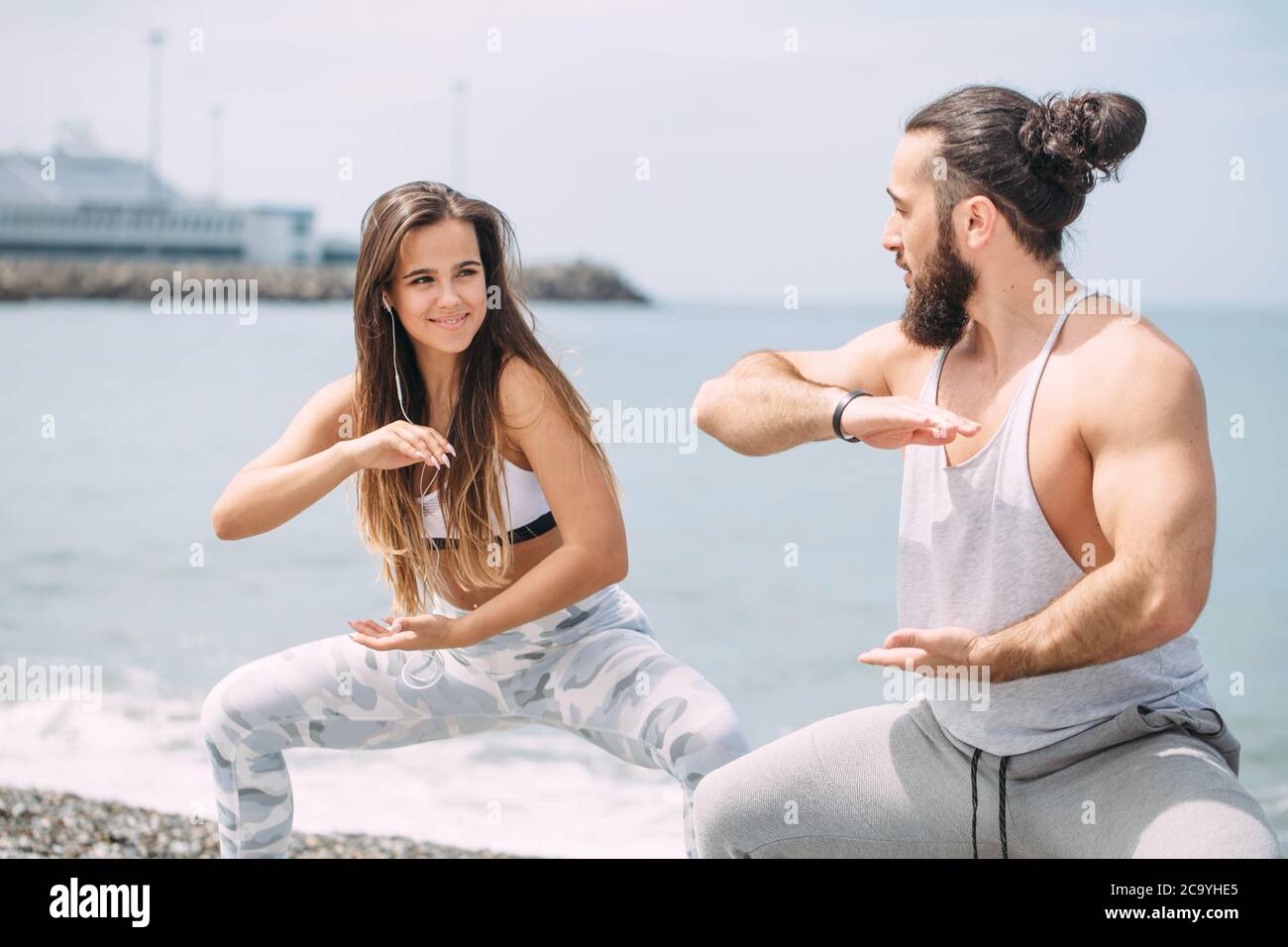 Pugile o combattente femminile professionista e il suo allenatore che si scaldano all'aperto, facendo taekwondo esercizio insieme sulla spiaggia di ghiaia oceano con mare surf A. Foto Stock