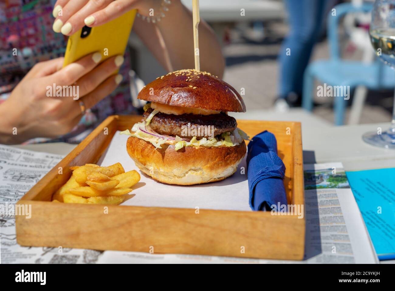 donna scatta una foto con il telefono sul suo hamburger per condividerla sui social media Foto Stock