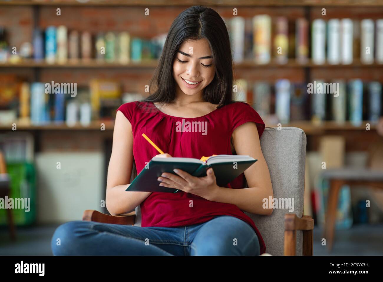 Ragazza studentesca asiatica seduta in biblioteca e prendendo appunti al blocco note Foto Stock