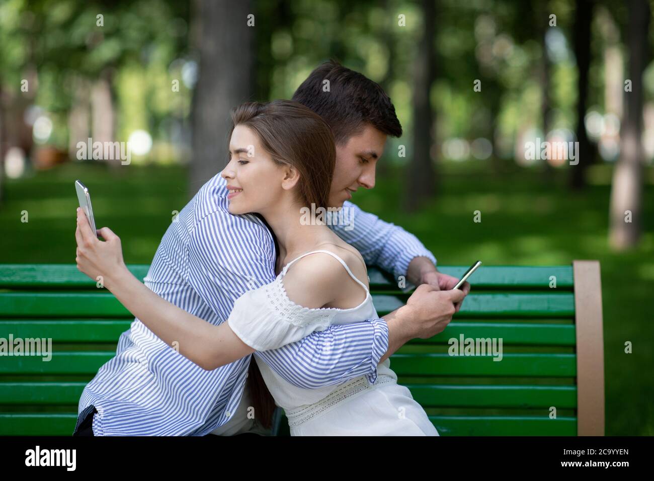 Dipendenza da Internet. Il ragazzo millenario e la sua fidanzata abbracciano e giocano sugli smartphone al parco Foto Stock