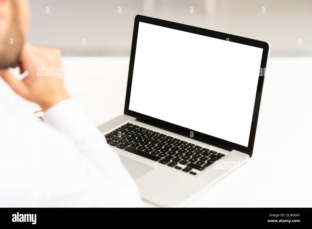 Foto con vista posteriore di un uomo d'affari che usa un notebook alla sua scrivania in un ufficio. Schermo intero bianco. Foto Stock