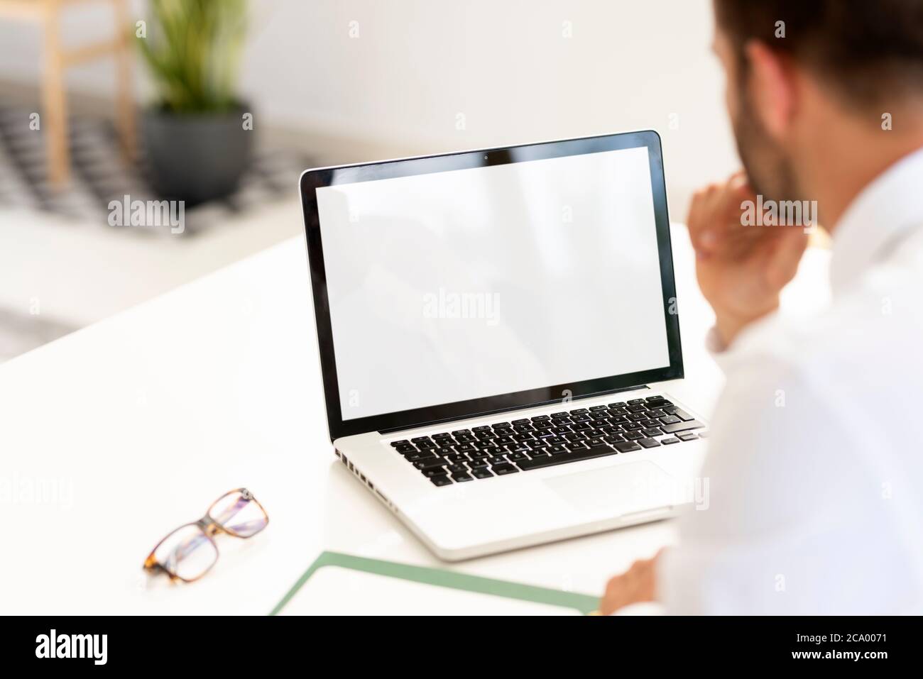 Foto con vista posteriore di un uomo d'affari che usa un notebook alla sua scrivania in un ufficio. Schermo intero bianco. Foto Stock