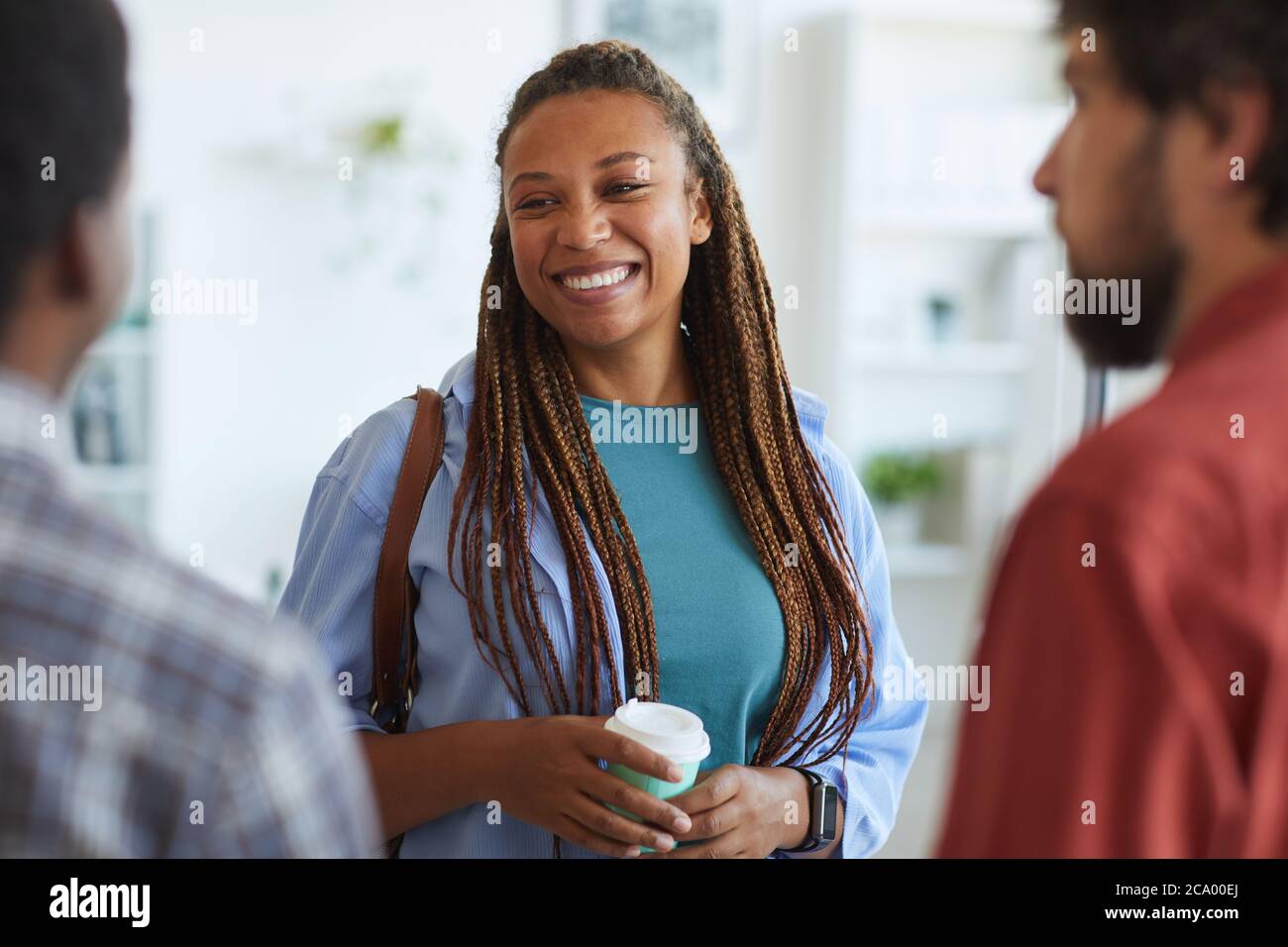 Vita in su ritratto della donna afroamericana contemporanea sorridente felice mentre parla con gli amici o i colleghi all'interno, copy space Foto Stock