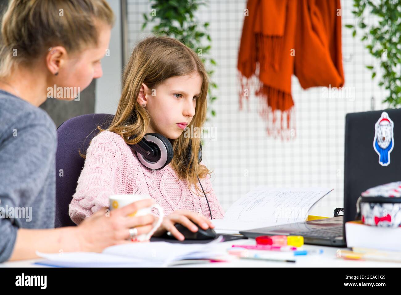 Giovane, ragazza bionda nel maglione rosa è confuso mentre fa le sue lezioni. Sua madre la sta aiutando. Homeschooling durante l'isolamento a casa. Foto Stock