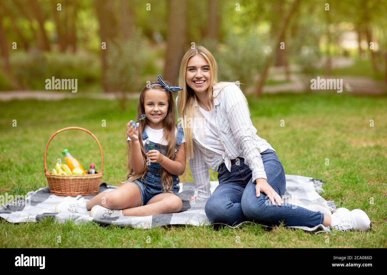 Madre e figlia soffiano bolle di sapone che si trovano a Park Foto Stock