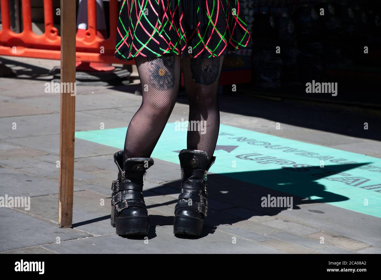 Un paio di gambe in calze a rete e stivali neri e chunky si trovano sul  marciapiede di Camden High Street Foto stock - Alamy