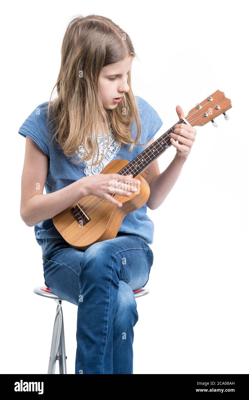 Teenage, ragazza bionda in T-shirt blu è seduta e sta giocando un concerto su ukulele strumento. Foto Stock