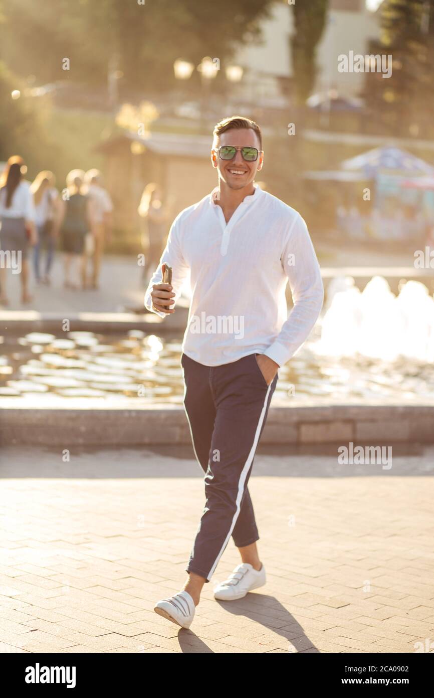 Bell'uomo biondo alla moda con camicia bianca e pantaloni sportivi alla  moda in piedi all'aperto nella città europea con fontana sullo sfondo Foto  stock - Alamy