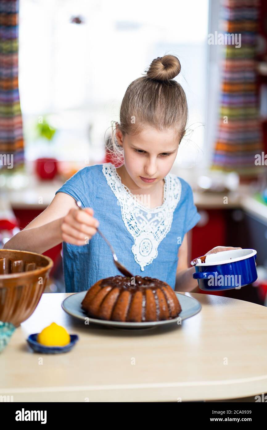 Il ragazzino sta facendo, facile da preparare e sano, torta di Pasqua fatta in casa - durante il soggiorno a casa. Sta decorando la torta con cioccolato fondente. Foto Stock