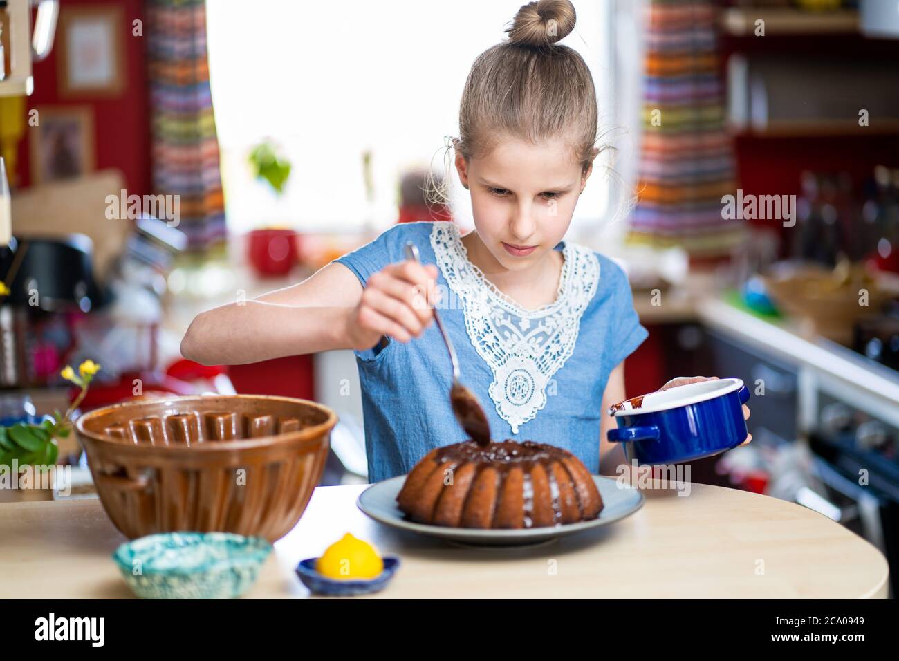 Giovane ragazza in T-shirt blu sta facendo, facile da preparare e sano, torta di Pasqua fatta in casa. Sta decorando la torta con cioccolato fondente. Foto Stock