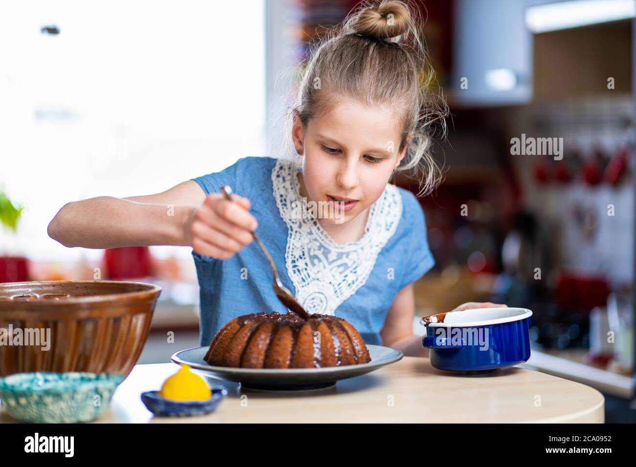 Il ragazzino in T-shirt blu sta facendo, facile da preparare e sano, torta di Pasqua fatta in casa. Sta decorando la torta con cioccolato fondente. Foto Stock