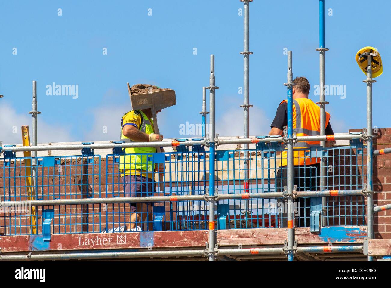 Costruttori che lavorano a Tarleton, Lancashire. Meteo Regno Unito. Caldo sole d'estate per lo sviluppo di nuova costruzione immobiliare nel nuovo Persimmon Housing Estate a Douglas Gardens. Uno sviluppo importante che può essere sospeso a seconda della gravità dell'imminente recessione. Si prevede che le contrazioni siano più incisive nel settore immobiliare privato (-42 per cento), nella riparazione di abitazioni commerciali e private, nella manutenzione e nel miglioramento , questi sono i settori più strettamente legati alla fiducia dei consumatori e delle imprese, che probabilmente saranno notevolmente intaccati dalla dissolvenza della sicurezza del lavoro e dall'aumento della disoccupazione. Foto Stock