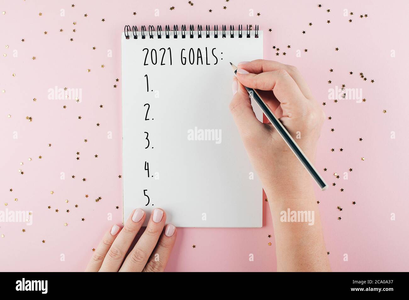 Felice anno nuovo 2021. La mano della donna che scrive 2020 obiettivi in taccuino decorato con le decorazioni di Natale sullo sfondo tricolore. Vista dall'alto, disposizione piatta Foto Stock
