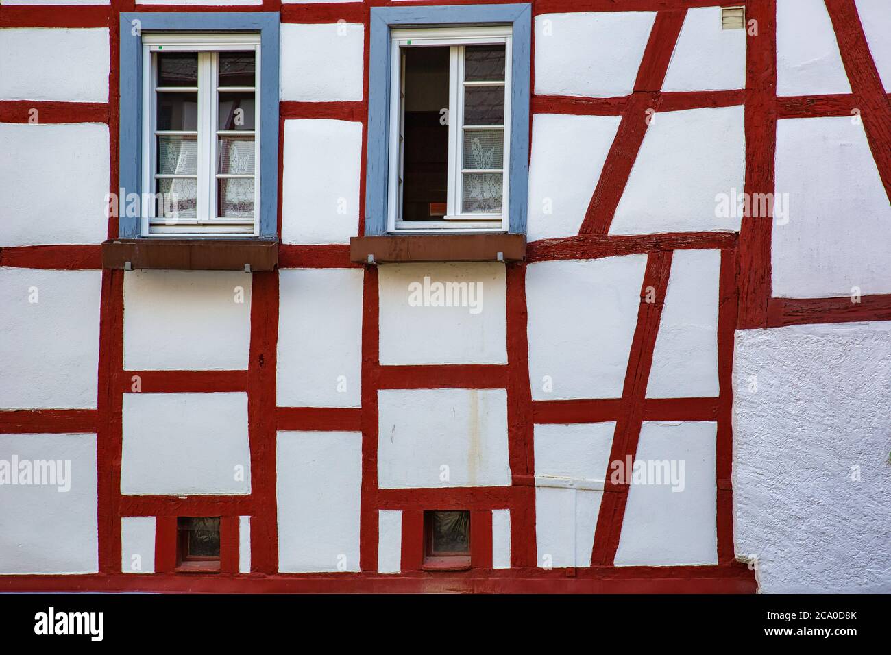 Parete bianca di un vecchio edificio a graticcio con travi in legno rosso e finestre blu Foto Stock