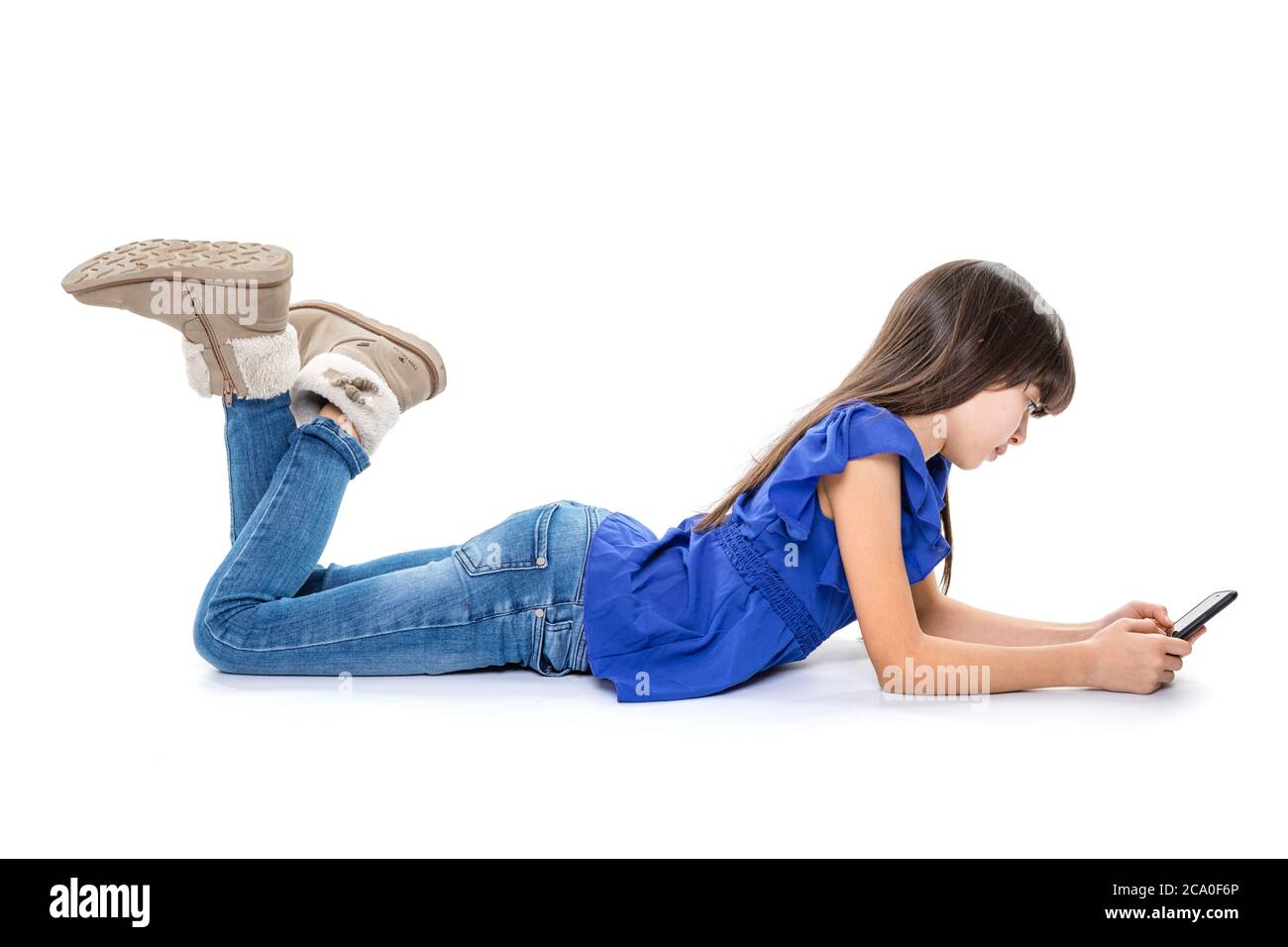 Bambina piccola bruna giovane in jeans e camicia blu giacente sul pavimento  su sfondo bianco isolato - e godendo il telefono cellulare. Sta giocando  Foto stock - Alamy
