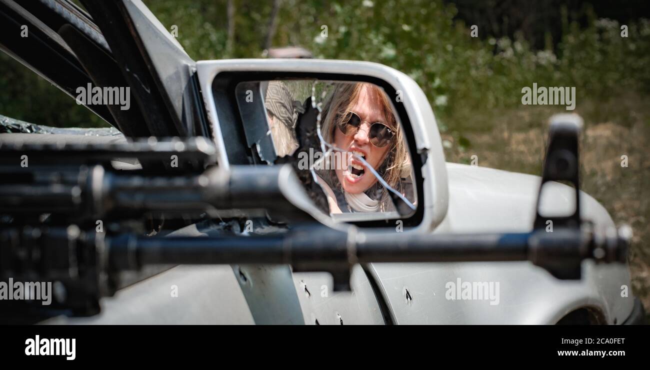 Vista astratta sullo specchio dell'aggressiva azione di un soldato femminile che spara dall'auto con fucile a macchina. Donna con arma. Femme fatale Foto Stock