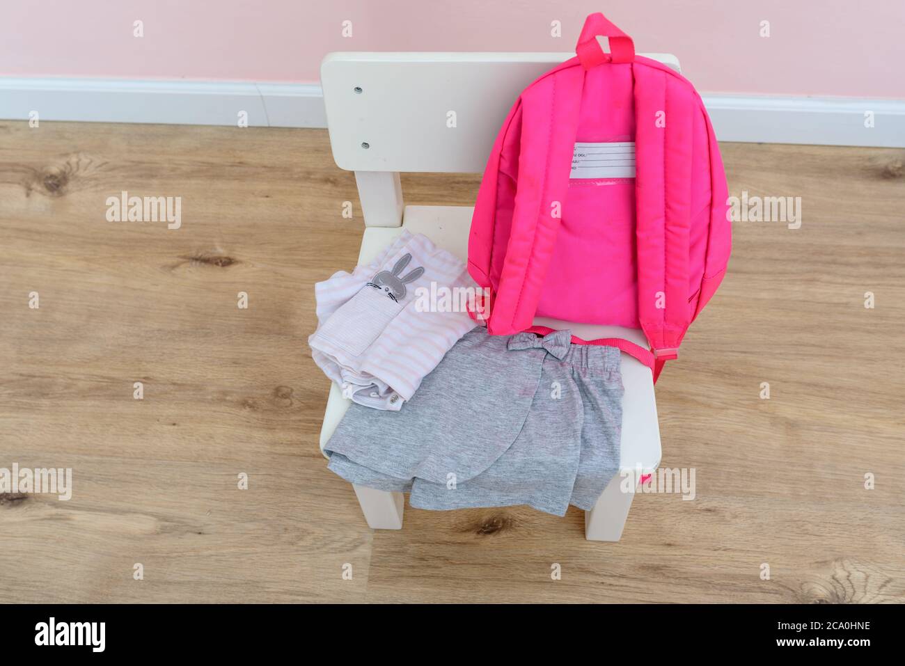 Forniture scolastiche : borsa e vestiti in camera per bambini su sedia in legno bianco. Mamma o genitori che preparano l'abito per la figlia da indossare il primo giorno di prescolare. Foto Stock